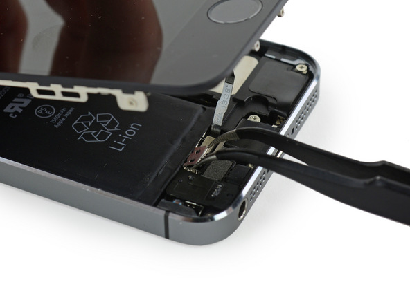 به منظور جا زدن براکت کانکتور دکمه هوم آیفون 5S ابتدا لبه های عرضی آن را با پنس بگیرید. لبه فوقانی آن را به سمت پایین شیب دهید و در شیاری قرار دهید که زیر باتری وجود دارد.