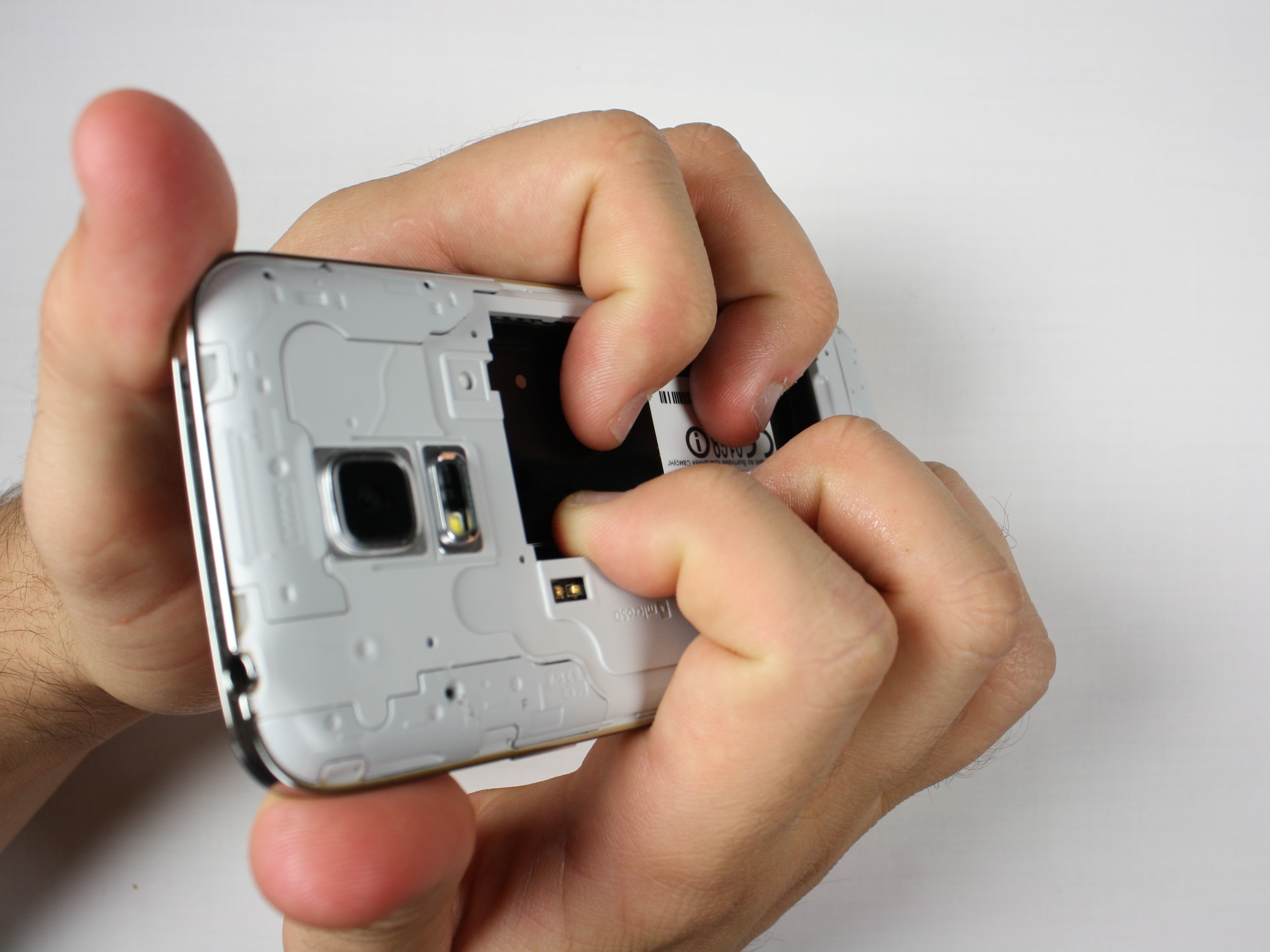 گلکسی اس 5 مینی تعمیری را مثل عکس اول در دستتان بگیرید. دقت کنید که انگشت اشاره و میانی دو دست شما باید در جایی از بدنه گوشی قرار بگیرند که باتری روی آن سوار می‌شود.