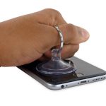 آیفون 6 اس پلاس تعمیری را روی میز کار یا یک سطح صاف قرار دهید. دست خود را روی صفحه نمایش آیفون بگذارید و با انگشت (مثل عکس) دستگیره ساکشن کاپ را محکم بگیرید. با نیروی یکنواخت ساکشن کاپ را به سمت بالا بکشید و به صورت همزمان کف دستتان را روی صفحه نمایش گوشی تکیه‌گاه کنید. به تدریج نیروی کششی اعمالی را افزایش دهید تا در لبه زیرین قاب آیفون تعمیری یک شکاف باریک ایجاد شود.