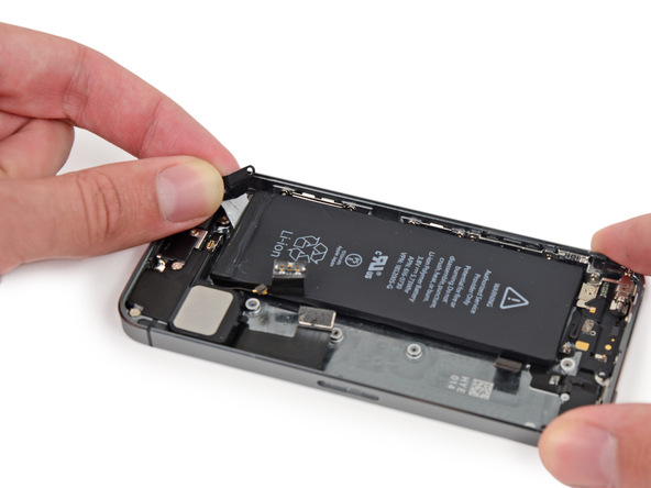 دومین چسب نگهدارنده باتری آیفون 5s تعمیری را هم دقیقا مثل چسب اول باز کنید. با این تفاوت که این بار باید سعی کنید چسب را به لبه سمت چپ باتری هدایت نمایید و از این بخش خارج کنید.